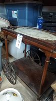 Full view of the wood tea cart with glass top showing overall condition, broken handle, and lower shelf.