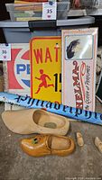 Image showing the vintage metal tin signs including Pepsi, Thelma Perfumes, and pedestrian crossing sign along with two wooden decorative clogs and a rolled Philadelphia poster.