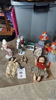 Wide shot showing multiple vintage dolls, Dept. 56 and Goebel Christmas figurines arranged on floor.