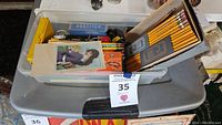 Top view showing several boxes and loose vintage stationary items including pencils, staples, erasers, sharpener, and a stapler inside a plastic storage bin.