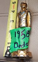 Front view of the 1958 Dodge Man metal ornament showing the figure and green label with handwritten date and brand.
