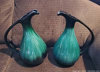 Pair of green and black BMP ceramic jugs or vases on a brown textured surface, showing full front view of both items.