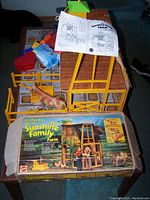 Top view of the assembled cardboard barn and plastic frame, includes plastic cow figure, instruction manual, and original box with graphics.