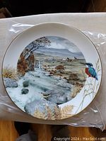 Front view photo of one collector plate showing a woodland stream and a kingfisher bird, approximately 9 inches diameter, gold rimmed.