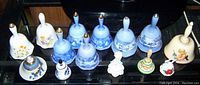 Overview of 13 china bells showing different designs including blue and white scenic patterns, floral motifs, and figurines