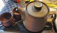 Photo of Denby stoneware teapot with lid and two matching cups on black surface.