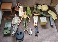 Three GI Joe action figures displayed with military-style furniture, cushions, and assorted weapons, on a carpeted surface