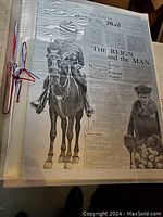 Close-up of laminated newspaper page showing British Royalty including a man on horseback and a woman in royal attire, secured in a cardboard binder