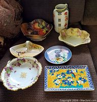 Full display of all seven ceramic and china items on a sofa showing variety and general condition.