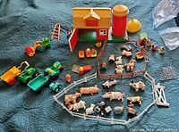 Overview of farm playset with barn, silo, multiple animals, tractors, fencing and farm accessories arranged on quilted surface.
