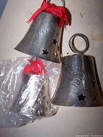 Close-up photo showing silver plate Christmas bells engraved 1990 and 1992 with red ribbon hangers, star cut-out designs, and some plastic wrapping.