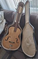 Full view of the acoustic archtop guitar inside a hard case with the case lid open showing the guitar body and neck.