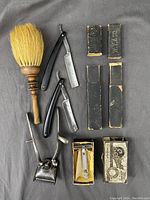 Photo shows entire antique barber tool lot including two straight razors with black handles in original cases, manual hair clippers, handheld razor in original box, horse hair neck brush with wooden handle.
