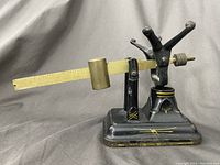Front angled view of black antique Fairbanks scale showing sliding yellow beam with cylindrical sliding weight and decorative markings on base.