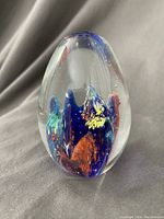 Front view of the clear glass paperweight showing colorful internal design of blue, orange, green, and yellow.