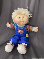 Front-facing view of Cabbage Patch doll wearing blue overalls and a striped shirt with yarn hair and white shoes