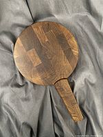 Top view of the round wooden cheese board with a handle, showing its dark patchwork wood grain pattern.