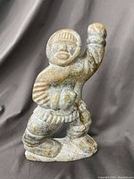 Soapstone carving of an Inuit figure standing with one arm raised, detailed carving of traditional clothing and facial features.