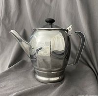 Side view of mid century stainless steel coffee pot with spout, handle, and black knob lid.