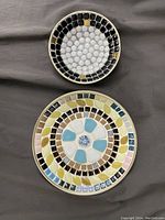 Top view of the 7.5 inch diameter plate showing pastel colored ceramic mosaic tiles arranged in a circular floral-like pattern. The 5 inch diameter bowl shown with black, white, and gold circular mosaic tiles.