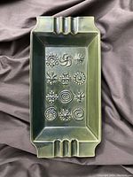 Top view of rectangular ashtray showing sage green glaze and abstract raised geometric pattern in the center, with cigarette rests on both ends.