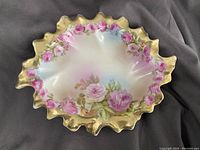 Top view of the Royal Vienna porcelain candy dish showing pink rose floral pattern around scalloped gold gilded edge on iridescent white background.