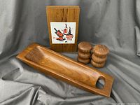 Photo showing all three items in the lot: the mid century tile plaque, the solid teak tray, and the pair of salt and pepper shakers.