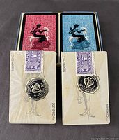 Two unopened decks of Claridge playing cards with red and blue backs, featuring a seated woman silhouette illustration and original tax seals on the Jokers.