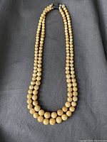 Photo of double strand vegetable ivory bead necklace laid flat on a gray fabric background to show the entirety of the necklace and bead detail.