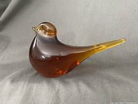 Right-side view of the amber glass bird paperweight showing smooth, amber color gradient and bird shape with long tail.