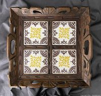 Front view of square wooden tray with carved edges and four ceramic tiles featuring yellow and brown decorative patterns.