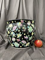 Front view of large vintage fish bowl planter showing black background with colorful Chinoiserie floral designs. Apple placed beside for scale.