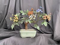 Front view of vintage glass floral bonsai sculpture showing multi-colored glass flowers, green leaves, brown trunk and pale green ceramic pot.
