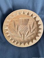 Top view showing detailed carved thistle design with surrounding geometric border on wooden press face.