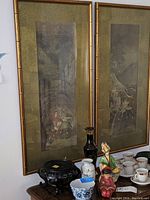 Pair of Asian style framed prints with bamboo look frames, showing partial details and other decorative items underneath.