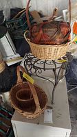 Photo showing wicker baskets stacked including darker and lighter colored baskets along with metal plant stand with four curved legs and rust spots