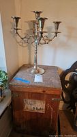 Photo of silverplated five-arm candelabra placed atop wooden storage crate, showing overall condition and size relationship.