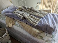 Two fur coats and one fur stole draped on bed, showing size and overall condition with visible damage at seams on sleeves and shoulders.