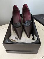 Gucci leather pointed-toe pumps in black box with tissue paper, shoes stuffed with black paper to maintain shape.