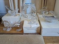 Full view of Lenox dolphin glass pieces arranged on white boxes showing different dolphin figurines, some marked with purple tape for nicks.