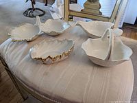 Four Lenox white porcelain candy dishes on a fabric surface showing shell shapes and basket-style with handle, all with gold trim.