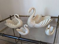 Four Lenox swan-shaped porcelain trinket holders arranged on a glass and metal table, showing overall size differences and design.