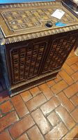 Front and top angled view of rectangular wooden hamper with carved geometric and floral patterns and a round cutout handle on top. Visible scratches and scuffs on the dark wood finish.