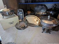 Wide angle photo of all metal serving items including platters, bowls, and warming dishes displayed on floor near furniture