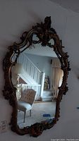Full view of tall wooden framed mirror with ornate decorative motifs including angel figure at top, showing reflection of interior room.