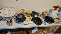 Wide view of all ceramic kitchenware and decor including mugs, teapot, spoon rests, colander, planter, ladybug timer.