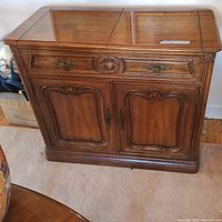 Front view of the wooden flip top server buffet showing drawer and double cabinet doors with carved details and metal handles.