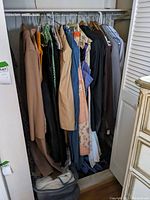 Closet with assortment of women's vintage clothing on hangers including coats, dresses, and blouses, showing condition and variety.