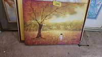 Framed painting displaying a large tree with orange and yellow fall foliage and a small figure of a child standing beneath it. Measurement tag '12x16' visible.