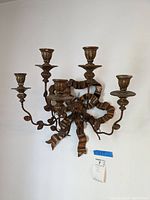 Front view of metal wall sconce with five candle holders and decorative bow design.